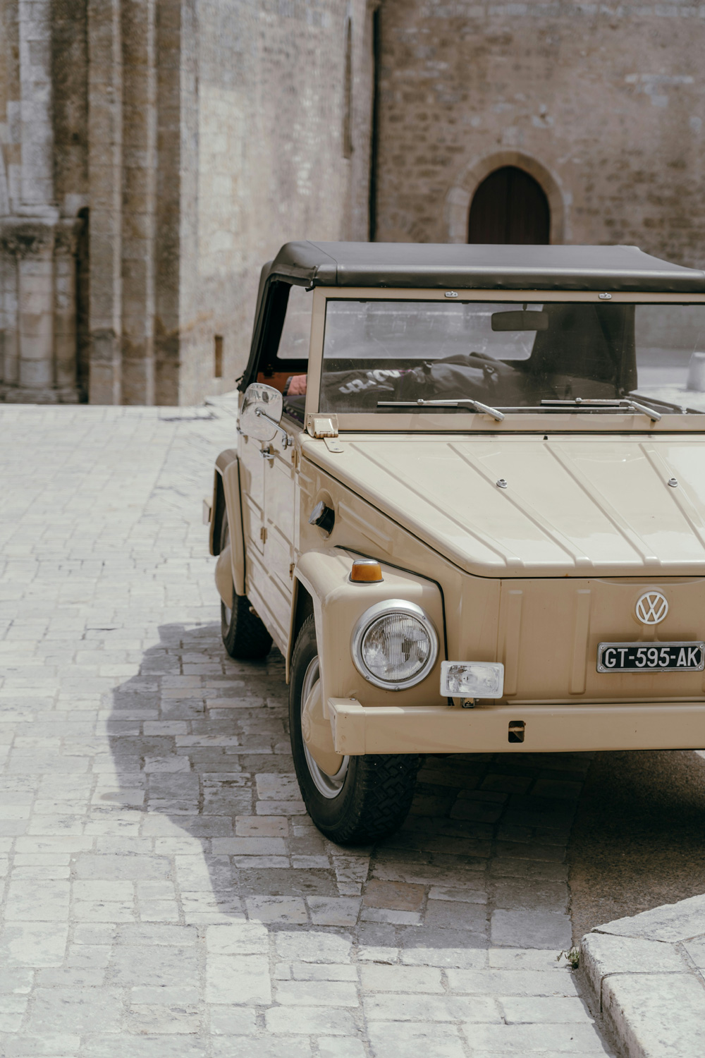 Beige vintage Volkswagen Thing parked on a cobblestone street in front of a stone building with an arched wooden door